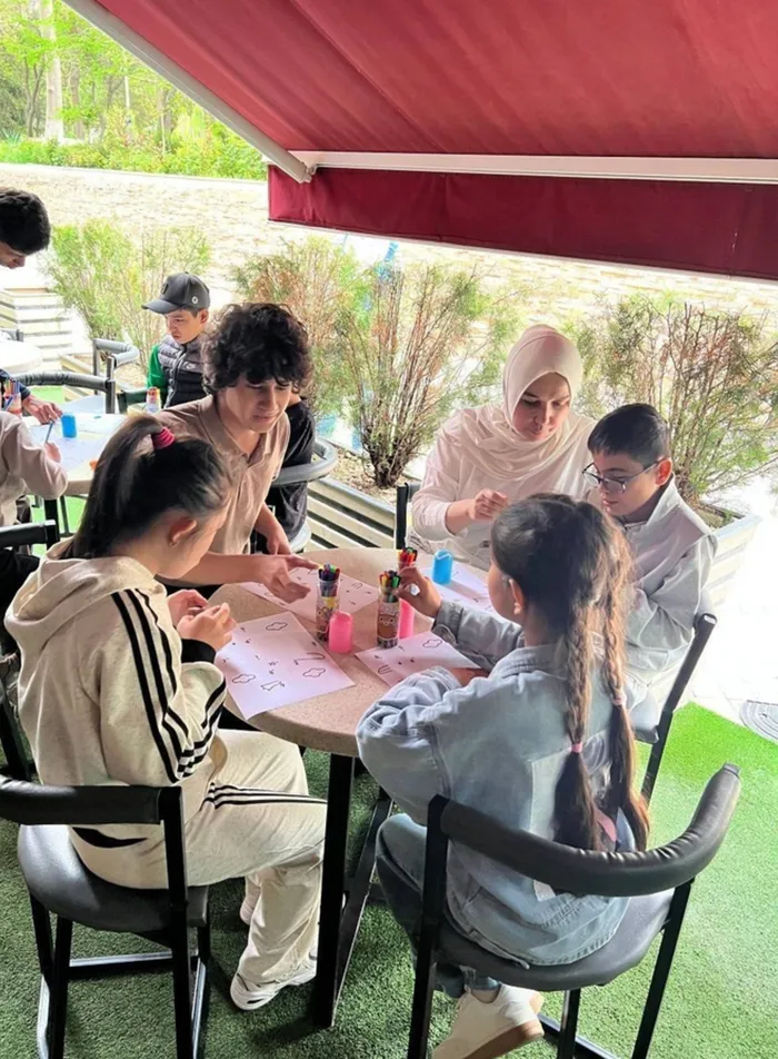 NeuroHope mashg‘ulotida bolalar ko‘ngillilar bilan stol atrofida topshiriq bajarmoqda